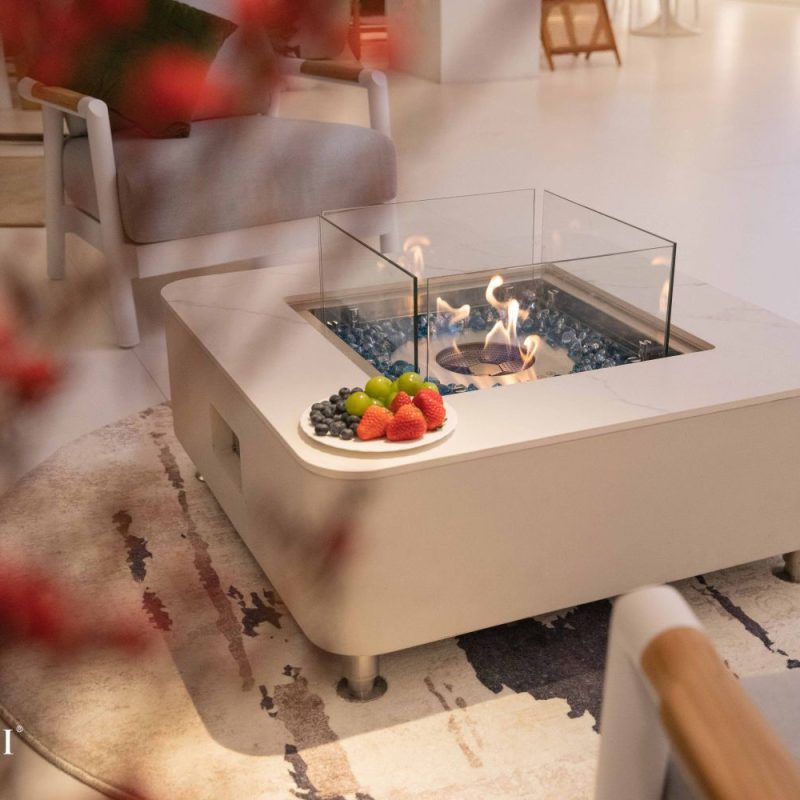 Elementi Aegean ethanol fire table styled indoors with marble porcelain top, glass flame guard, and fruit display on a modern coffee table.